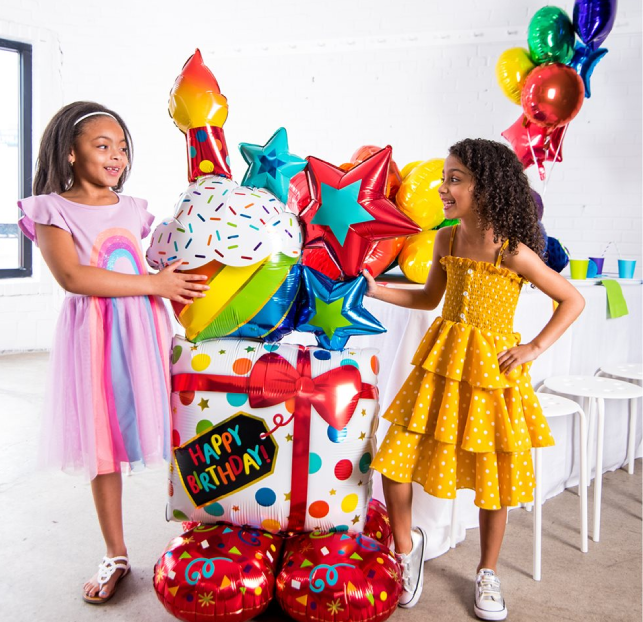 Two girls celebrating a colorful birthday party with balloons and gifts.